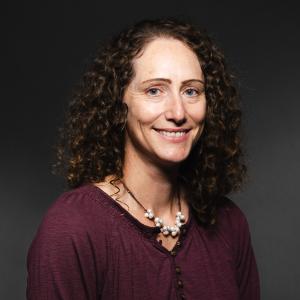 Liz Young wearing a maroon shirt and pearl necklace smiling for her headshot.