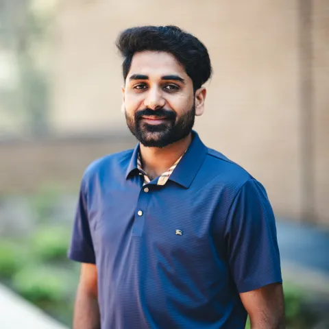 Adeel Hashmi standing in front of a building for his headshot wearing a blue pollo shirt.