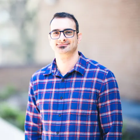 Amirhossein Zahmatkeshsaredorahi standing in front of a building for his headshot wearing a blue plaid shirt.