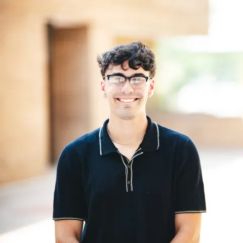 Benno Weidner wearing a bakck polo shirt and glasses smiling for his headshot in front of a brick building.