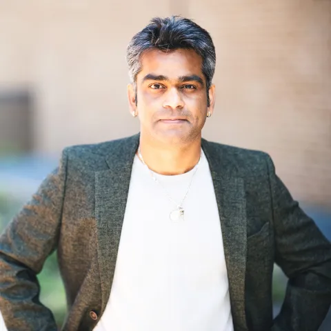 Bharath Kumar standing in front of a brick building for his headshot wearing a white shirt and suit jacket.