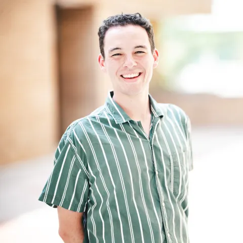 Brett Berger wearing a green and white striped shirt standing in front of a brick building for his headshot.