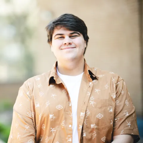 Chad Propst standing in front of a brick building for his headshot wearing an orange button button-up shirt.