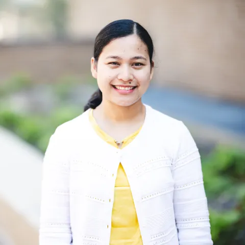Cherry Mae Ravidas standing in front of a brick building for her headshot wearing a yellow shirt and a white sweater.
