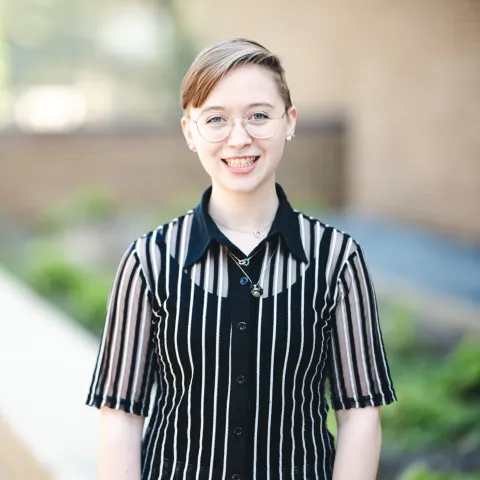 Cristabella Fortna wearing a white and black shirt smiling for her headshot outside.