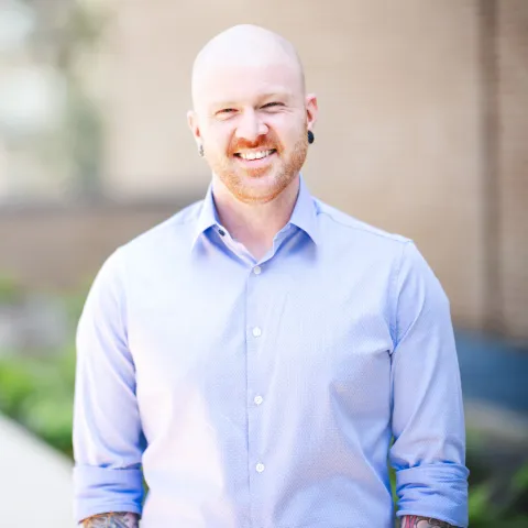 Dane Santa wearing a blue shirt smiling outside for a headshot.