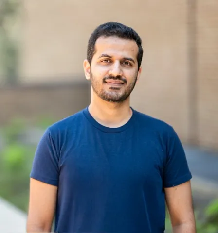 Graduate student Fareed Ul Haq Khan standing in front of brick building wearing a blue t-shirt.
