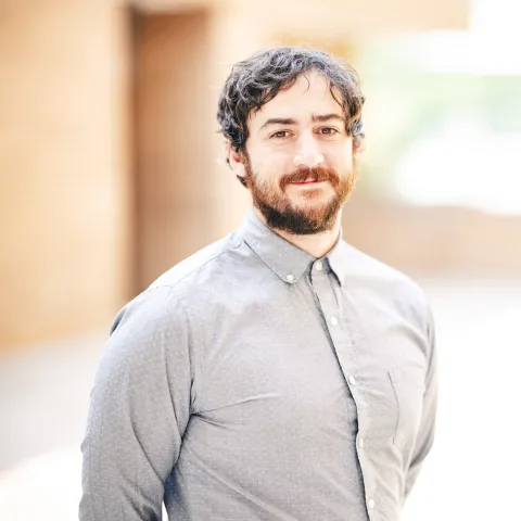 Jacob Atherly wearing a grey button-down shirt smiling for his headshot in front of a brick building.