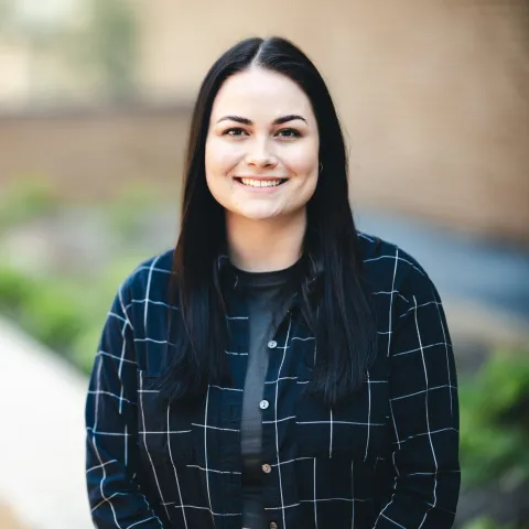 Jesika DeDonato wearing a flannel button up shirt smiling for her headshot outside.