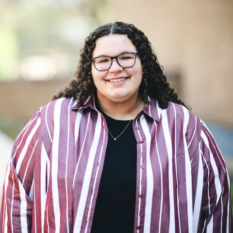 Katrina Brandmier wearing a red and white striped shirt smiling for her headshot outside.