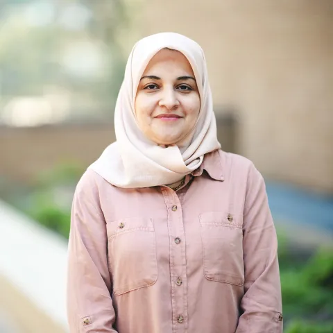 Khansaa Alshaloug wearing a pink shirt smiling for her headshot outside in front of a brick building.