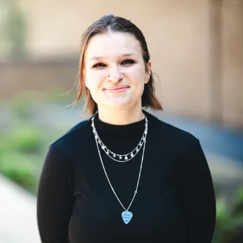 Leah Knepper wearing a black shirt and necklaces smiling for her headshot outside.