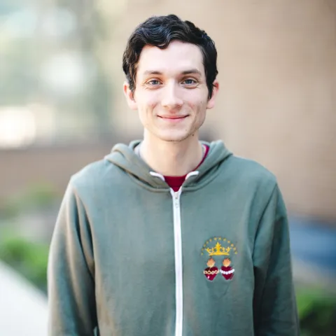 Nicholas Manidis standing in front of a brick building for his headshot wearing a green zip up hoodie.