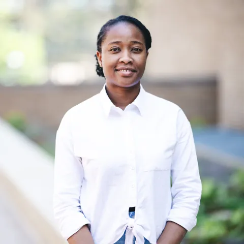 Ruth Ebubechukwu standing in front of a brick building for her headshot wearing a white button-up shirt.