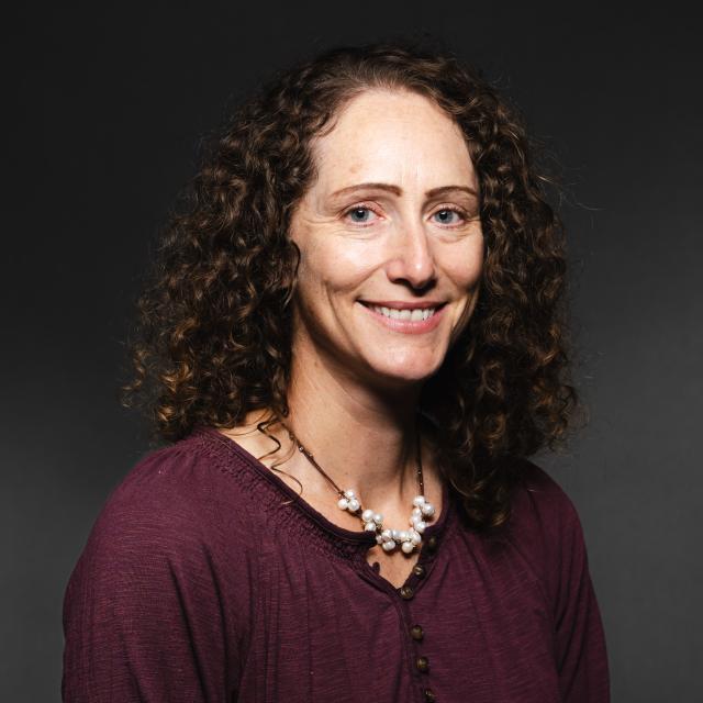 Liz Young wearing a maroon shirt and pearl necklace smiling for her headshot.