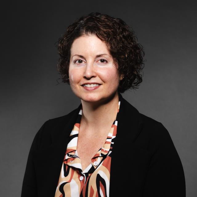 Monica Rieth wearing a colorful shirt and black sweater smiling for her headshot.