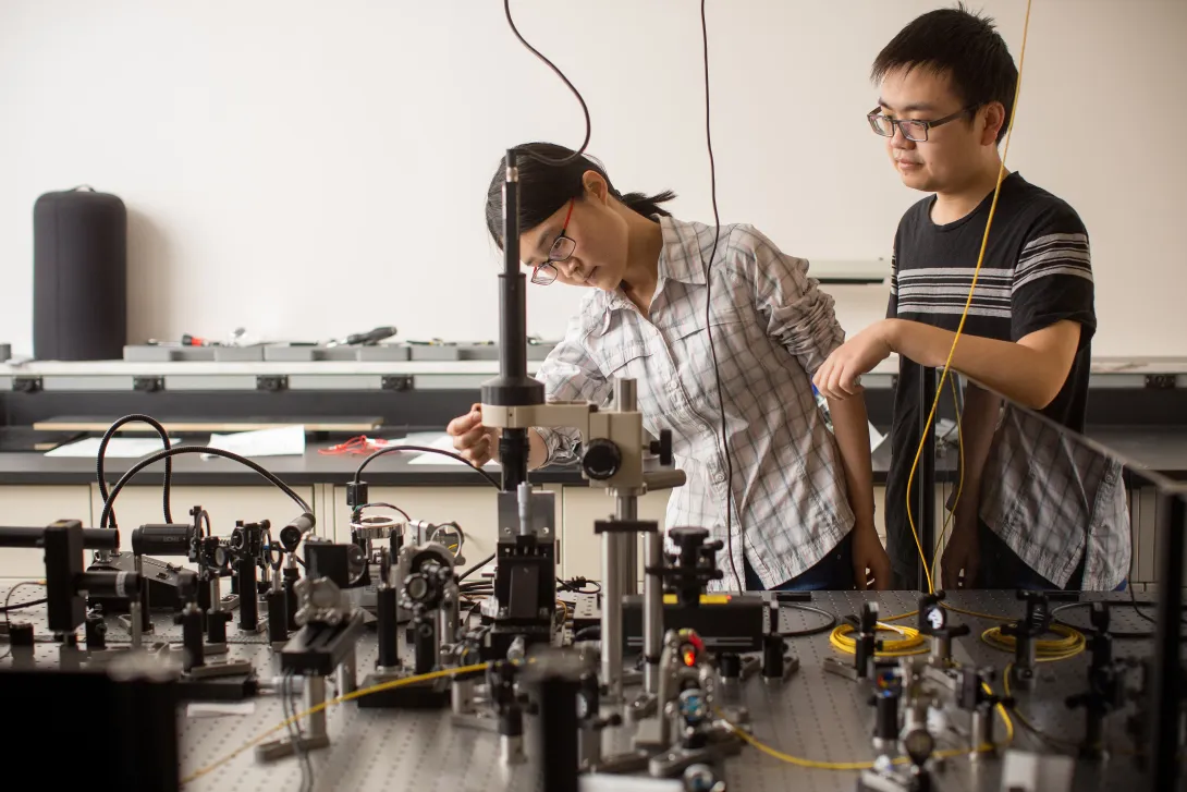 A female and male graduate student working in a lab with lasers